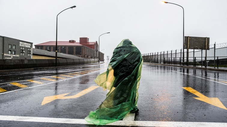 A man stands in the rain to ask for money at a traffic light during a cold front in Woodstock, Cape Town, South Africa, July 9, 2024.